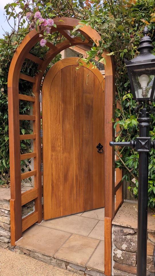 Arched Iroko garden gate shown open within the bespoke timber frame